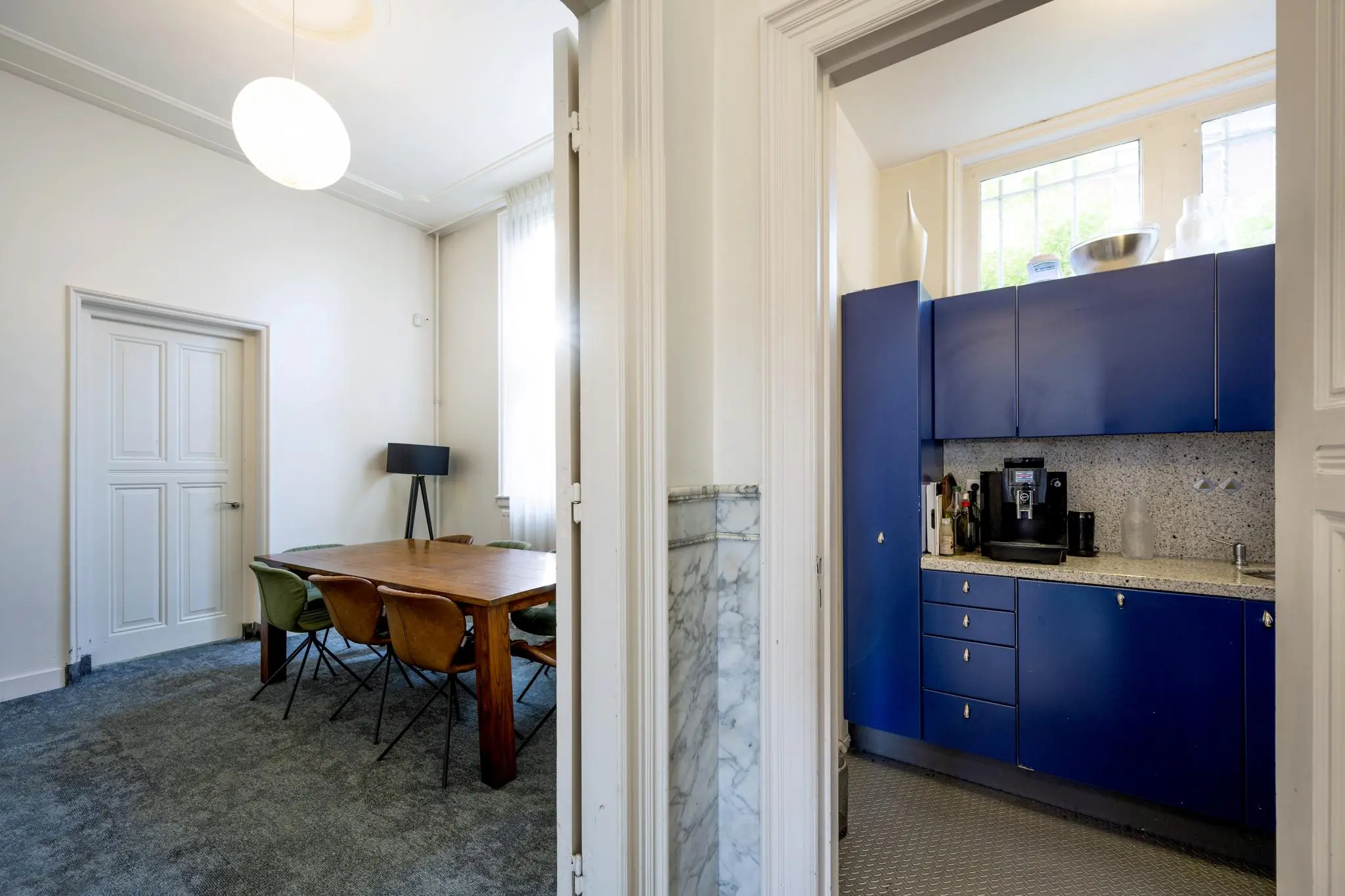 Zicht op een eetkamer met houten tafel en een aangrenzende keuken met blauwe kastjes in een woning aan de Van Eedenstraat.